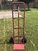 Front view of red metal dolly with tall back and flat base plate on grass.
