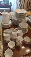 Wide view showing grouped plates, cups, coffee pot, creamer, gravy boat, and sugar bowl with visible chips on some items.