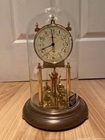 Front view of quartz mantle clock under glass dome, showing clock face and pendulum balls.