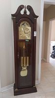 Front view of wooden grandfather clock with bonnet top, glass door, brass weights and pendulum