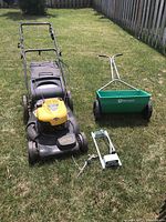 Wide shot showing mower, spreader, and accessory on grass