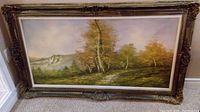 Front view of framed autumn landscape painting with distant mountains, trees and path.