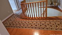 L-shaped carpet runner positioned around wooden stair railing and hardwood floor.