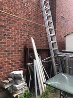 Wide view showing scaffolding frames, pipes and an extension ladder leaning against brick wall