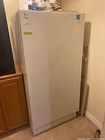 White Maytag upright freezer standing against a wall near wooden cabinetry, displaying minor surface marks and overall good shape