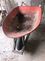 Front perspective of the wheelbarrow showing red metal tub interior with dirt and a black single rubber tire.