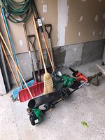 Overall view of yard tools including shovels, rakes, brooms, blower, Weed Eater