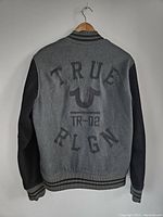 Back view of True Religion varsity jacket showing embroidered logo and text on grey wool body and black leather sleeves