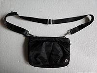 Front view of small black Lululemon bag with strap laid out showing logo and pleated fabric detail.