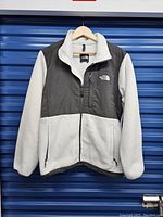 Front view of men's two-tone fleece jacket hanging on a hanger showing full front zipper, color blocking in light and dark gray.