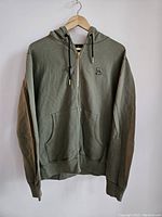 Front full view of olive green zip-up OVO hoodie with hood, zipper, pockets, and logo on chest.