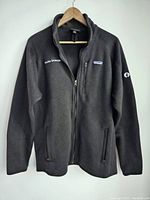 Front view of a black Patagonia fleece jacket with full front zipper and zippered pockets, showing Oculus Browser text on right chest and Facebook logo patch on left sleeve.