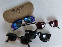Four pairs of sunglasses arranged with a textured Maui Jim branded case in the background. Blue mirrored lenses pair is prominent.