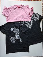 Three t-shirts laid flat showing a pink Supreme t-shirt and two black Marcelo Burlon x Disney graphic tees