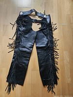Full view of black leather chaps showing fringe detail and overall condition