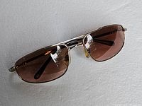 Front angled view of the titanium frame sunglasses with brown lenses on a white textured background.