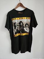 Full front view of black T-shirt with photo of three reggae artists framed by colorful geometric border.