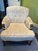Front view of vintage upholstered armchair showcasing cream damask fabric and wooden leg and armrest details