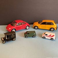 Five model cars on display: two larger front sedans (red Beetle and yellow PT Cruiser) and three smaller metal vans including a black vintage delivery van, olive green military van and white van with red markings.
