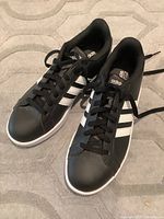 Pair of black Adidas sneakers showing top and side views with white stripes and black laces.