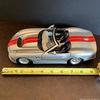 Side view showing scale next to tape measure, silver Shelby model car with red stripes and open doors.