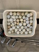 White plastic container filled with many used golf balls showing signs of dirt and wear.
