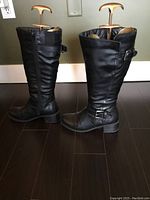 Side view of pair of black leather women's boots showing buckles, ruched design, and wide leg opening.