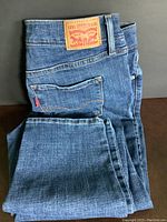 Folded blue denim Levi's jeans showing the back pocket with red Levi's tab and leather brand patch on waistband.