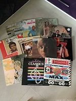 Photo of 15 vinyl albums showing various artist covers including a woman in a red dress, a close-up female portrait, and colorful illustrated albums.