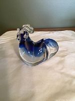 Blue glass rooster paperweight shown on a white surface with visible shape and coloring.
