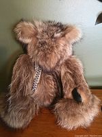 Stuffed bear with long brown fur shown from front angle, posing on a wooden surface. Moveable limbs evident with leather paws visible.