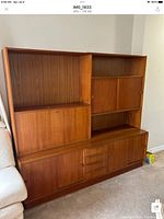 Full view of teak wall unit showing upper shelving, sliding doors, central drawers and lower cabinets against neutral wall
