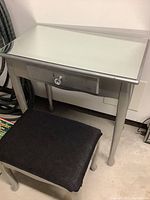 Mirrored vanity desk with drawer and upholstered stool from a side angle