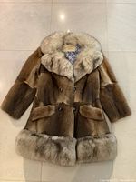 Front view of the brown vintage fur car coat with lighter fur collar and trim, double-breasted buttons, front flap pockets.