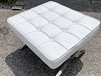 White tufted ottoman at front angle on asphalt