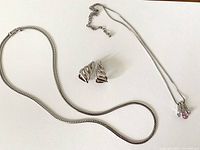 Two silver-tone necklaces and a pair of silver-tone clip-on earrings laid out on a white background.