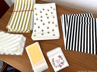 A variety of gift wrapping bags stacked on a table including gold and white stripes, gold polka dots on white, black and white stripes, clear with white stripes, and floral motif bags.