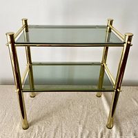 Front view of brass tubular frame side table with smoked glass shelves on fabric surface, showing two-tier design.
