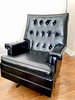 Front angled view of vintage black faux leather swivel chair showing tufted backrest and padded armrests