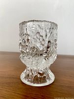 Small clear glass tumbler with textured bubbled surface and pedestal base pictured front on wooden surface.