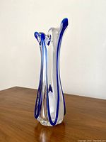 Clear glass Murano art glass vase with cobalt blue swirl detail on a wooden surface, showing side view with three curved extensions at top.
