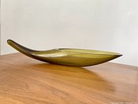 Side view of the smoked glass planter showing its sleek curved form and slightly raised handle end, resting on a wood surface.