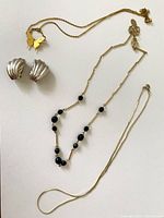 Photo of two necklaces and a pair of silver-tone clip-on earrings on a white surface.