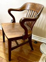 Side angle view of solid oak vintage chair showing curved armrest and backrest slats.