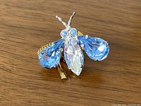 Close-up view of the vintage bee pin showing the blue and clear rhinestones and gold-tone metal details.