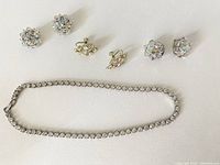 Photo showing the rhinestone tennis necklace laid out flat with three pairs of clip-on earrings arranged above it.