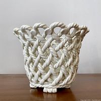 Front view of vintage white glazed ceramic planter shaped like woven basket with a twisted rope design and scalloped top edge