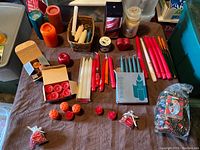 Overview of assorted candles of various shapes, colors and sizes on table, including taper candles, pillar candles, votive and tealight candles, some boxed