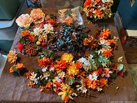 Wide overhead view of assorted silk flowers and leaves in various colors and types spread out on a brown surface.