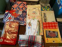 Full view of assorted holiday tablecloths including vinyl and fabric, various patterns including patriotic and Christmas themes